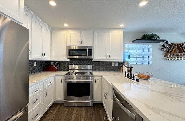 kitchen featuring dark wood-style flooring, a sink, white cabinets, appliances with stainless steel finishes, and light stone countertops