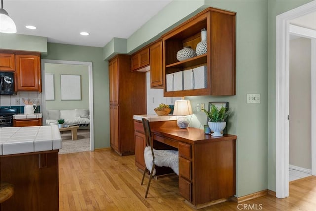 kitchen with tasteful backsplash, tile countertops, brown cabinets, light wood-type flooring, and black microwave