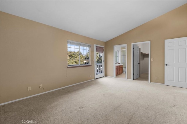 unfurnished bedroom featuring baseboards, light colored carpet, lofted ceiling, ensuite bathroom, and a spacious closet