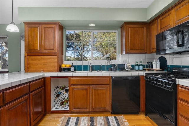 kitchen with black appliances, light wood-type flooring, brown cabinets, and decorative backsplash