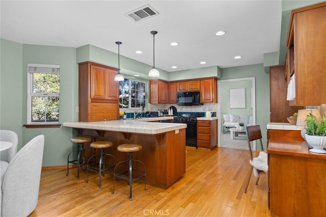 kitchen featuring tile countertops, a peninsula, visible vents, a kitchen breakfast bar, and black appliances