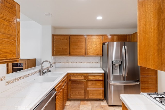 kitchen featuring tasteful backsplash, tile counters, brown cabinets, stainless steel appliances, and a sink