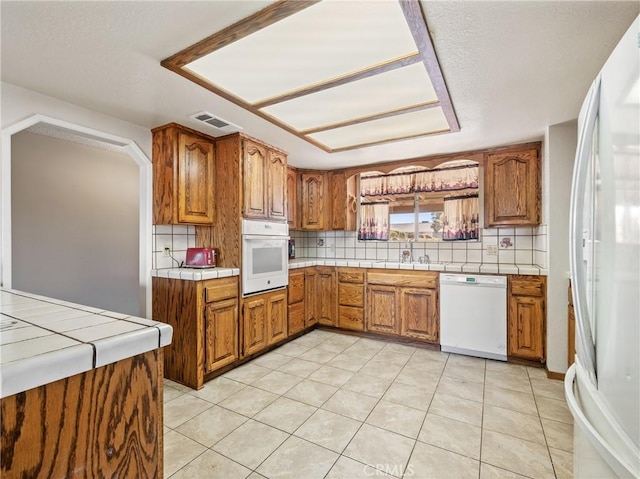 kitchen featuring brown cabinetry, white appliances, visible vents, and tasteful backsplash