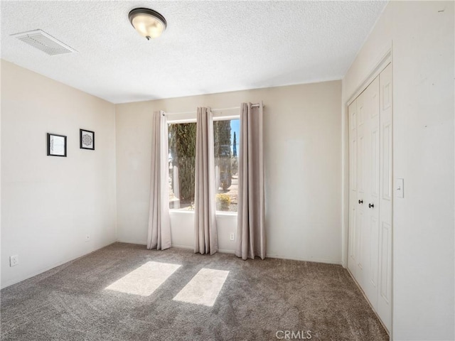 spare room with a textured ceiling, carpet, and visible vents