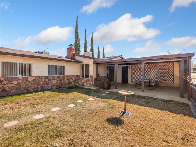 back of property featuring a patio, stone siding, a chimney, a yard, and stucco siding