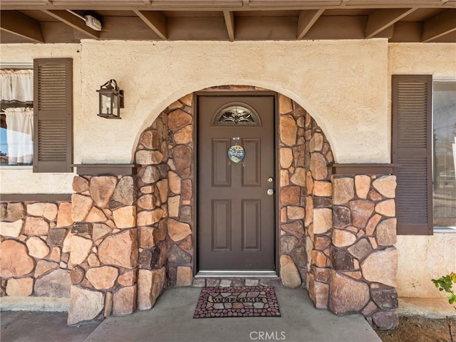 view of exterior entry featuring stone siding and stucco siding