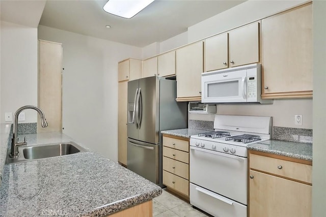 kitchen with light brown cabinets, white appliances, and a sink