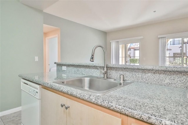 kitchen featuring a healthy amount of sunlight, white dishwasher, a sink, and light brown cabinetry