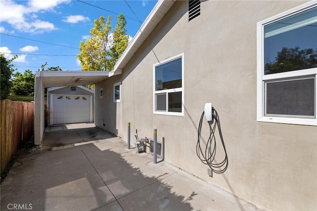 view of side of home featuring stucco siding, fence, a carport, driveway, and an outdoor structure