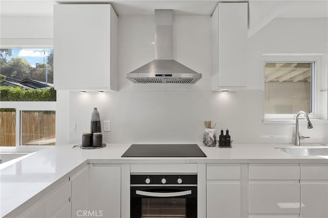 kitchen with black appliances, wall chimney exhaust hood, a sink, and white cabinetry