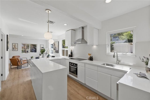 kitchen with visible vents, oven, black electric stovetop, wall chimney range hood, and a sink