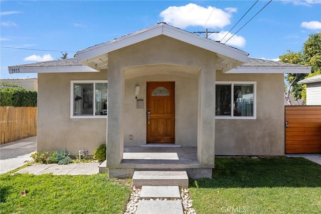 doorway to property featuring a yard, fence, and stucco siding