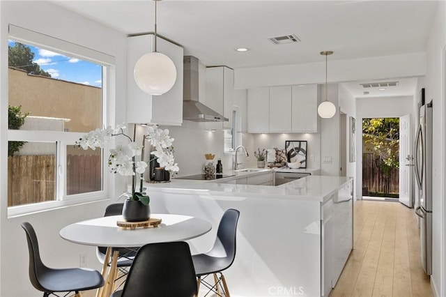 kitchen featuring wall chimney exhaust hood, modern cabinets, freestanding refrigerator, black electric stovetop, and light countertops