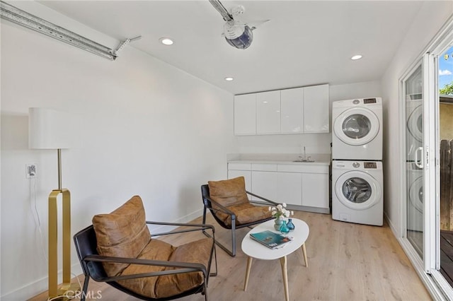 laundry area featuring light wood finished floors, stacked washer and dryer, a sink, laundry area, and baseboards