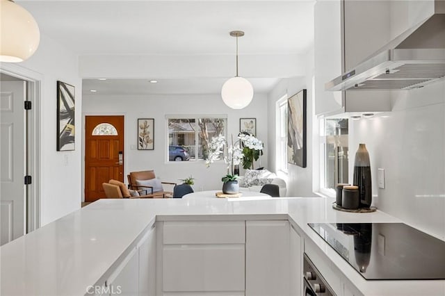 kitchen with black electric stovetop, white cabinets, open floor plan, light countertops, and wall chimney exhaust hood