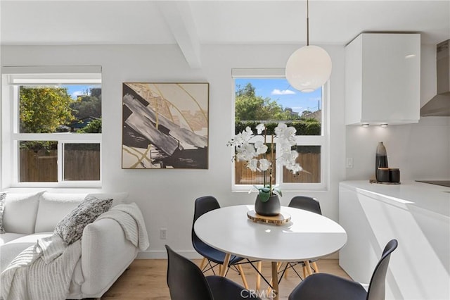 dining space featuring beamed ceiling, light wood-type flooring, a wealth of natural light, and baseboards