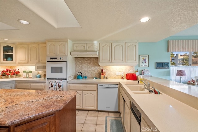 kitchen featuring tasteful backsplash, light tile patterned flooring, a sink, white appliances, and under cabinet range hood