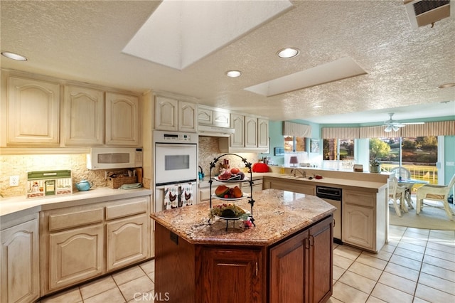 kitchen with a peninsula, white appliances, visible vents, a center island, and tasteful backsplash