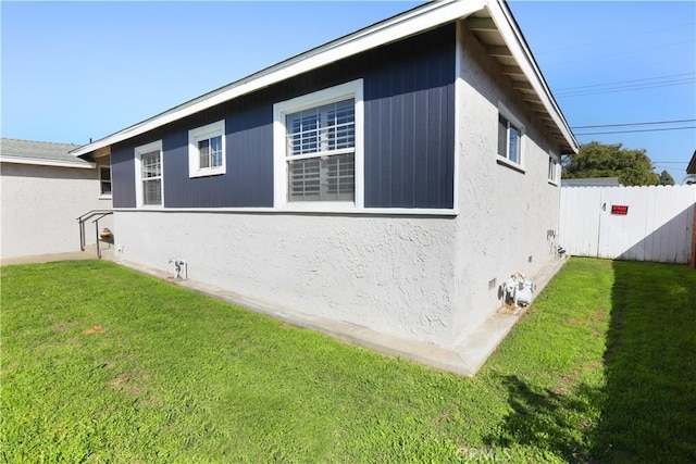 view of side of property featuring a lawn, fence, and stucco siding