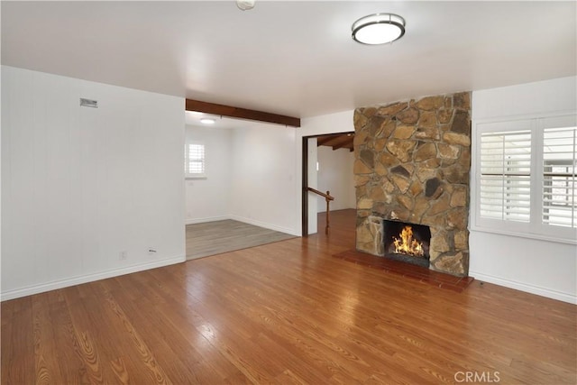 unfurnished living room featuring a fireplace, baseboards, wood finished floors, and beamed ceiling