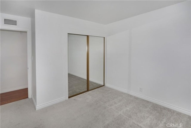 unfurnished bedroom with a closet, visible vents, light carpet, and baseboards