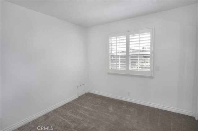 empty room featuring baseboards and dark colored carpet