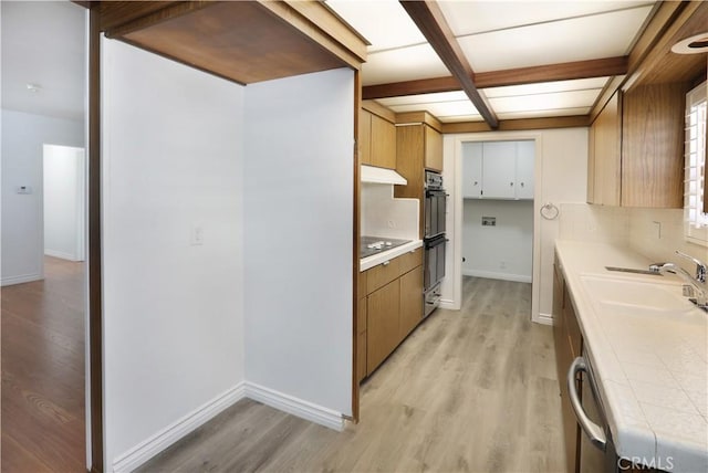 kitchen with brown cabinets, light wood finished floors, light countertops, and a sink