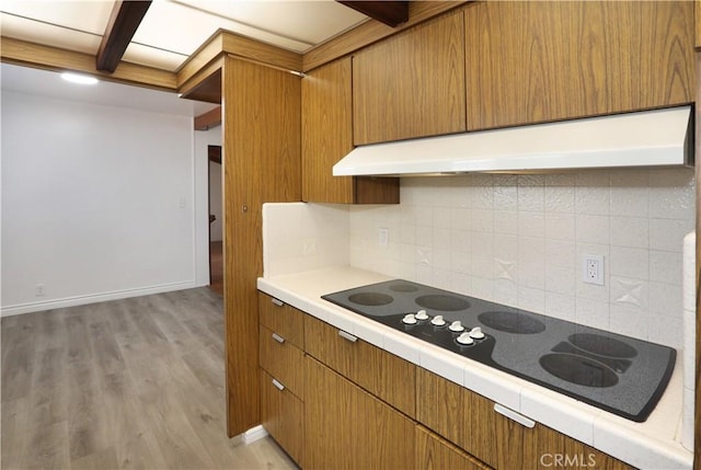 kitchen featuring light wood-style floors, brown cabinets, black electric stovetop, light countertops, and under cabinet range hood