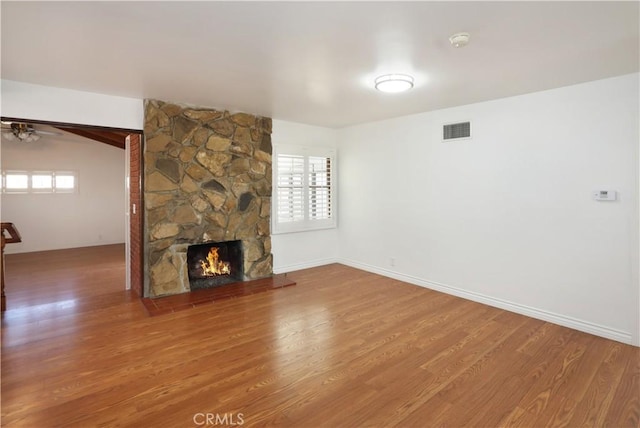 unfurnished living room with plenty of natural light, visible vents, wood finished floors, and a stone fireplace