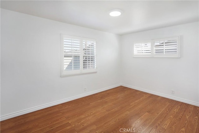 unfurnished room featuring plenty of natural light, baseboards, and wood finished floors