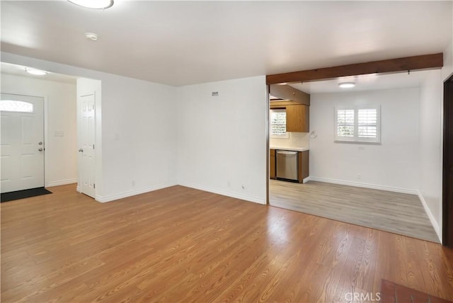 unfurnished living room with baseboards, beamed ceiling, and light wood finished floors