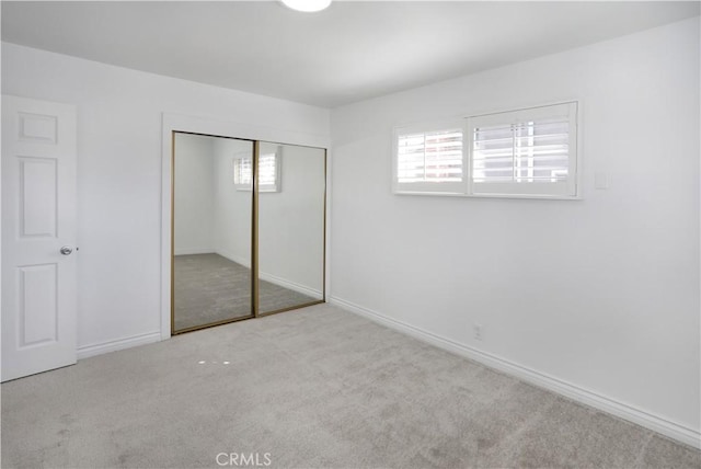 unfurnished bedroom featuring a closet, light colored carpet, and baseboards