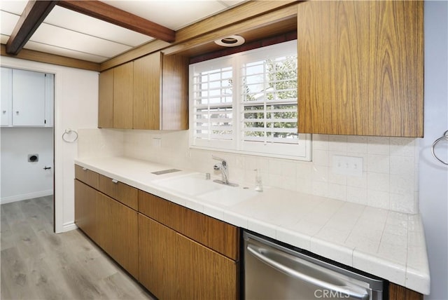 kitchen with decorative backsplash, beamed ceiling, stainless steel dishwasher, light wood-style floors, and a sink