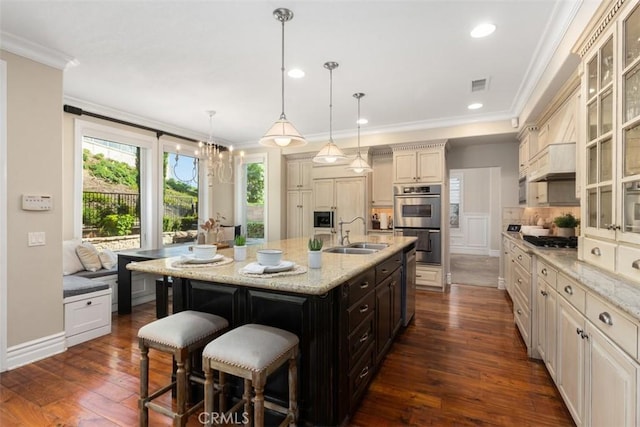 kitchen featuring a kitchen island with sink, a sink, visible vents, hanging light fixtures, and glass insert cabinets