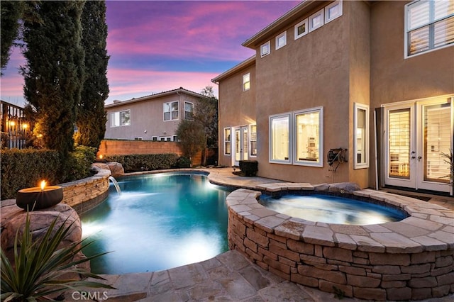 pool at dusk with a pool with connected hot tub, fence, and french doors