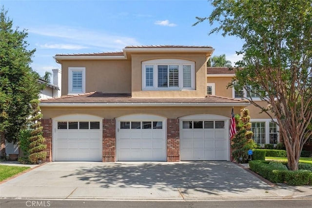 view of front facade featuring driveway, brick siding, an attached garage, and stucco siding