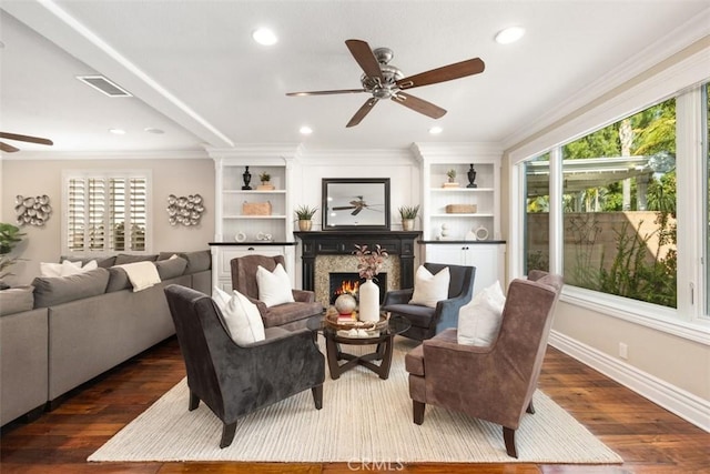 living room with a wealth of natural light, dark wood finished floors, crown molding, and a lit fireplace