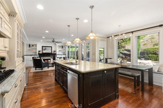 kitchen featuring an island with sink, decorative light fixtures, light stone countertops, stainless steel appliances, and a sink