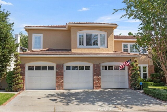 view of front of property featuring an attached garage, stucco siding, concrete driveway, and brick siding