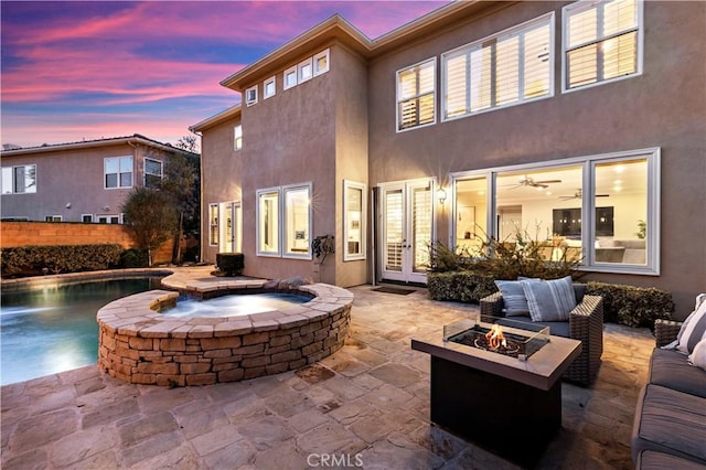 back of house at dusk with french doors, an outdoor living space with a fire pit, a patio, and stucco siding