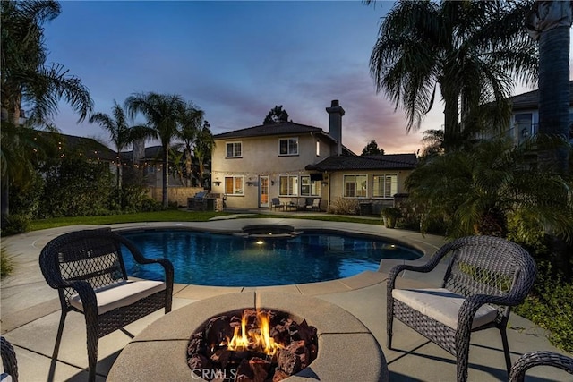 pool at dusk with a fire pit, a patio area, and a pool with connected hot tub