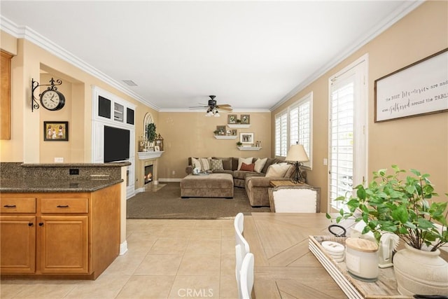 living room with baseboards, a fireplace with flush hearth, ceiling fan, ornamental molding, and light tile patterned flooring