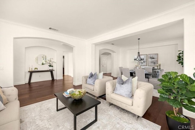 living room featuring arched walkways, a chandelier, wood finished floors, visible vents, and crown molding