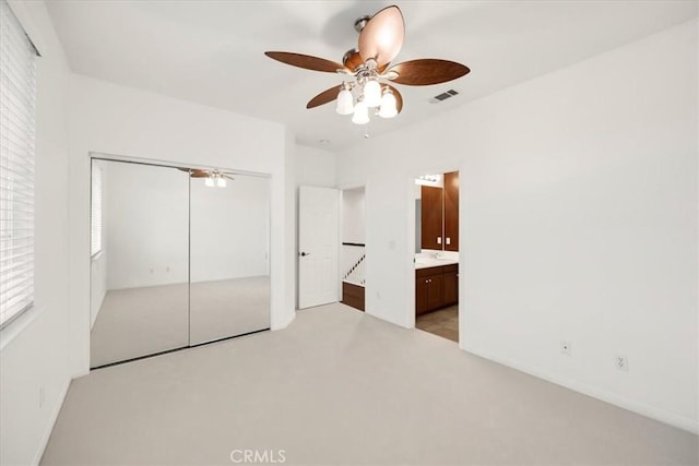 unfurnished bedroom with visible vents, a ceiling fan, light colored carpet, ensuite bathroom, and a closet