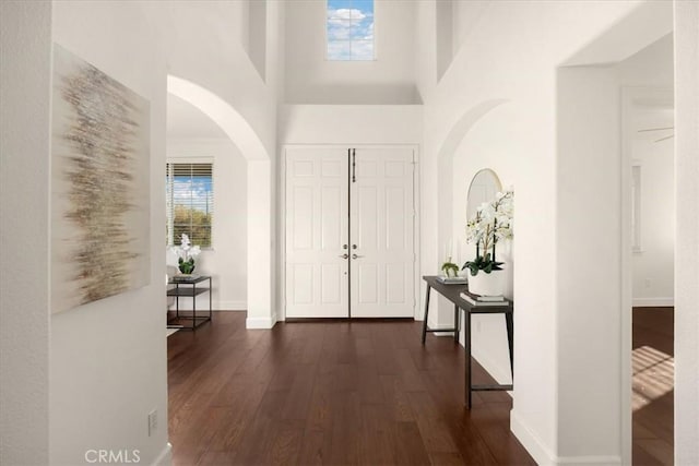 foyer with dark wood-style floors, arched walkways, baseboards, and a high ceiling