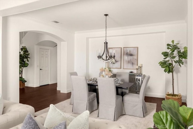 dining space featuring arched walkways, a notable chandelier, wood finished floors, visible vents, and crown molding