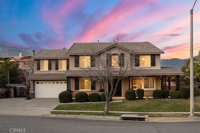 view of front of home with driveway, stucco siding, an attached garage, a mountain view, and a front yard