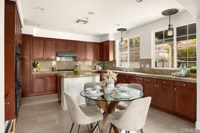 kitchen with under cabinet range hood, tasteful backsplash, visible vents, and decorative light fixtures