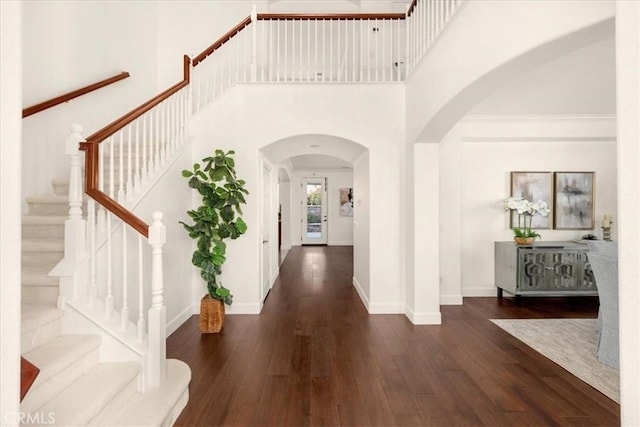 foyer with arched walkways, a high ceiling, dark wood-style flooring, and baseboards