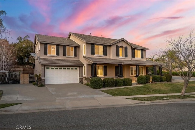 view of front facade with a yard, stucco siding, concrete driveway, covered porch, and an attached garage